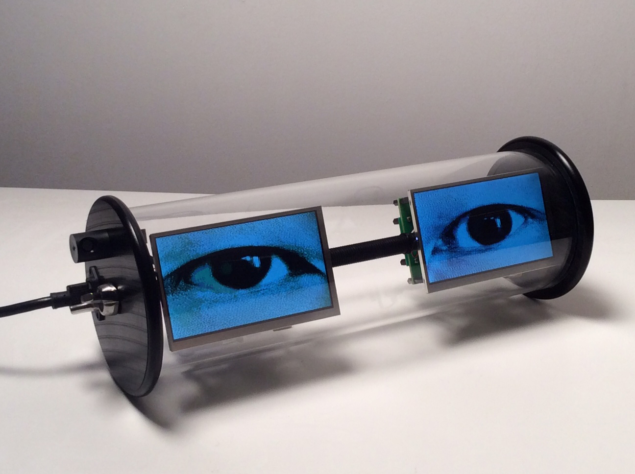 A digital art installation with two videos of eyes on blue screens encapsulated in a glass tube.