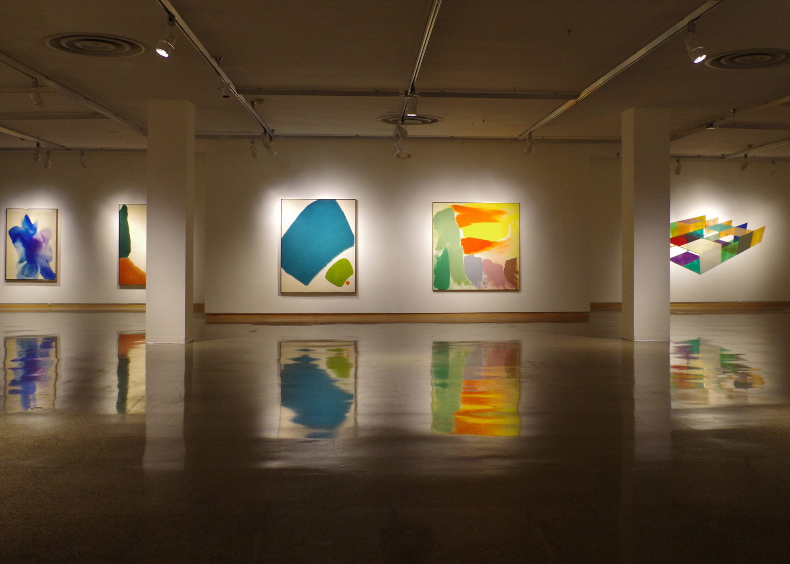 A gallery interior with abstract art installed, lit by spotlights.