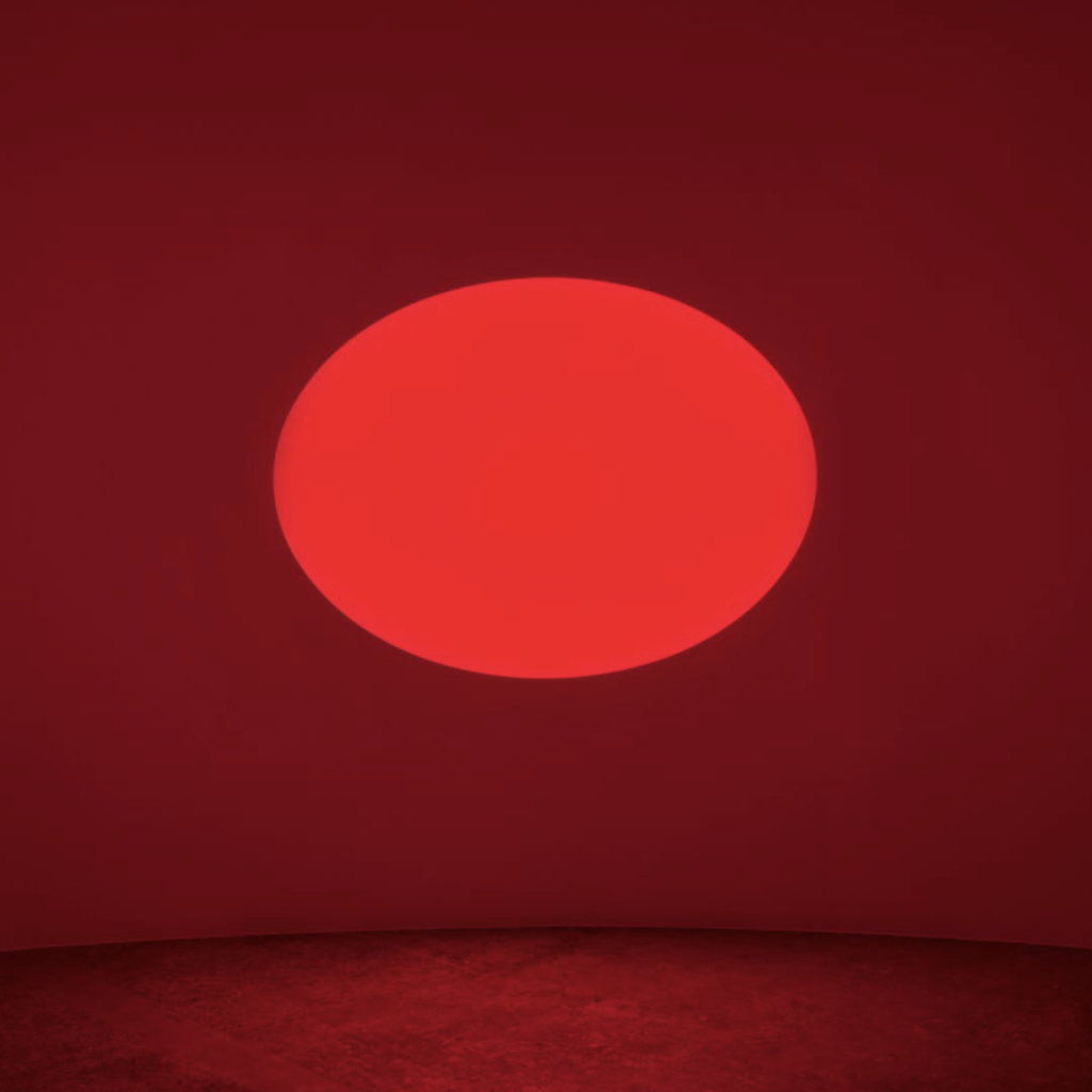 An artwork composed of an elliptical aperture in a wall with a glowing red light emitting, turning the entire space red.