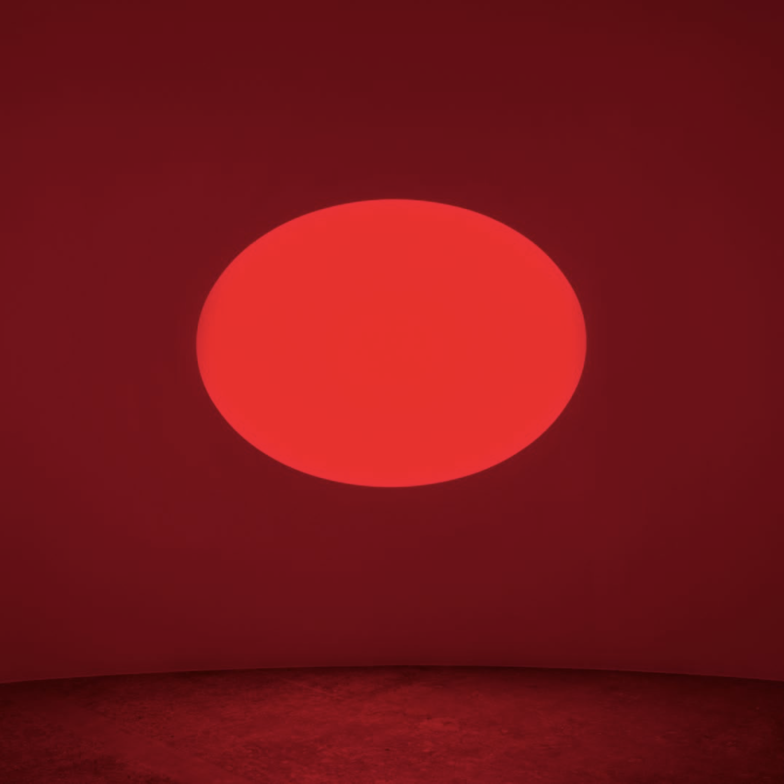 An artwork composed of an elliptical aperture in a wall with a glowing red light emitting, turning the entire space red.